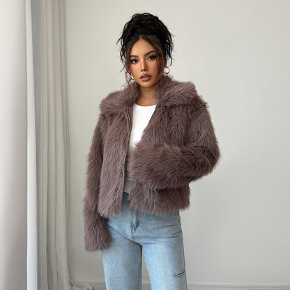 Woman with curly updo wearing mauve faux fur jacket over white top and light blue jeans indoors