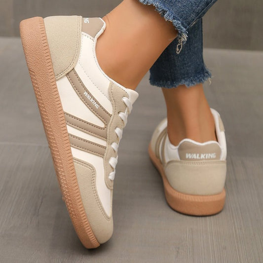 Beige and white casual walking shoes with gum soles worn with frayed hem blue jeans on a wooden floor