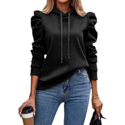 Woman wearing black puff sleeve hoodie with drawstrings and blue jeans holding coffee cup and jacket